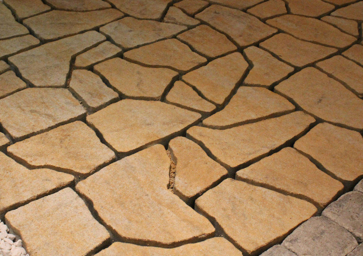 Nahaufnahme von sandfarbenen Betonsteinen in unterschiedlichen Formen, die eine eben verlegte Bodenfl?che bilden. 